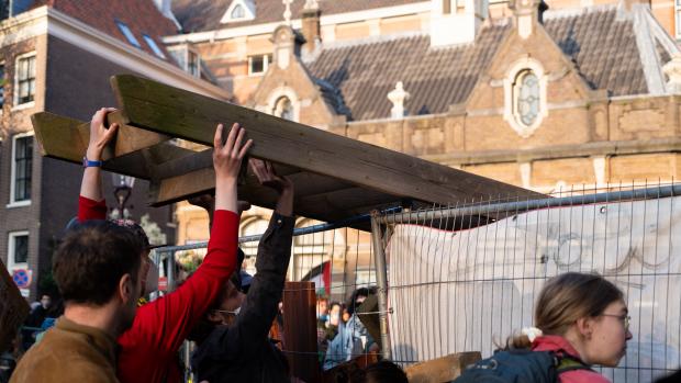 Overleg door driehoek
Demonstranten zijn rondom de Oudemanhuispoort bezig bakstenen uit de grond te halen om de barricaden te verstevigen. Ook zijn er meerdere bustes, meubels en brandblussers uit de voormalige Academische Club gehaald, die nu bezet is door de demonstranten. &nbsp;Zo&rsquo;n tweehonderd omstanders staan toe te kijken buiten de barricaden. Enkele politiebusjes staan ook op het terrein, met agenten die de boel in de gaten houden. Volgens het Parool zou er nu een overleg gaande zijn tussen de driehoek, om de situatie te bespreken.