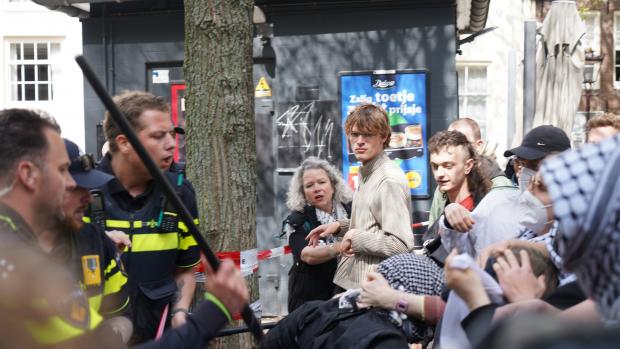  Flessen waterEen stuk of tien demonstranten probeerde langs de politieafzetting te komen en gooide flessen water en sap richting het bordes. De aanwezige agenten vormden een linie om te voorkomen dat de demonstranten konden doorbreken. Een van de activisten krijgt een klap met een wapenstok, waarop de groep actievoerders in woedend geschreeuw losbarst.&nbsp;Even later verschijnen er bezetters op het dak van het Maagdenhuis. Er volgt een luid applaus van inmiddels ruim tachtig demonstranten op het Spui. De bezetters op het dak onthullen een groot spandoek met &lsquo;Cut ties with genocide&rsquo;.&nbsp;